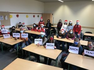 Die Klasse 8c hält mit Weihnachtsmützen bekleidet die Worte „Das Elo wünscht frohe Weihnachten!“ hoch.